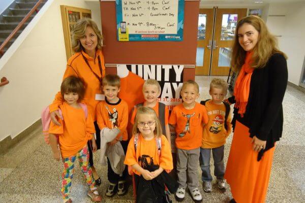 A group of teachers and their students all wearing orange