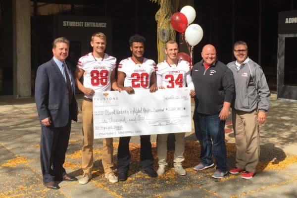 Football players and coaches holding a giant check