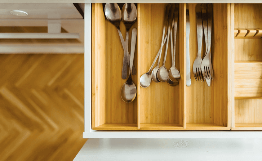 Silverware organized in a brown wooden drawer.